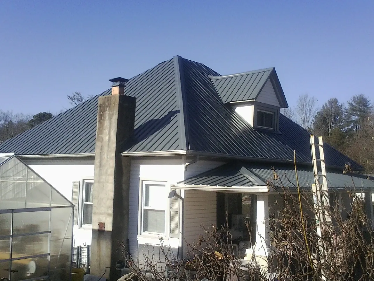 Dark blue standing seam metal roof on a white farmhouse with dormer — Slate & Tile Roof Repair by Roofing Brothers in Clute