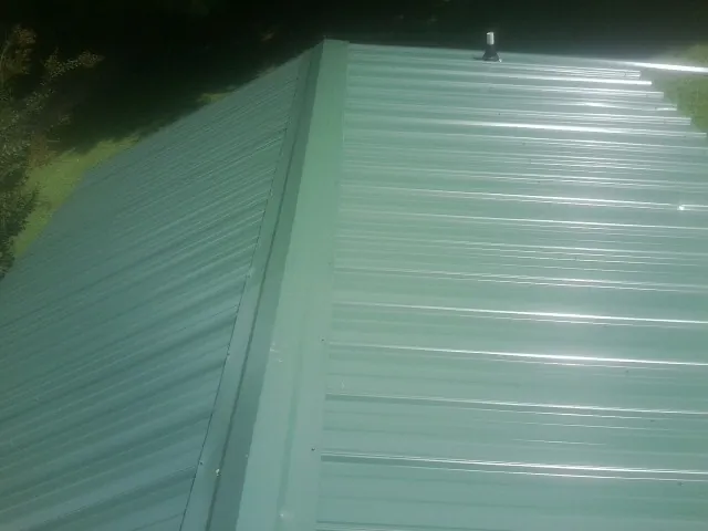 New green metal panels meeting at the ridge of a roof — Flat Roof Repair work by our crew in Clute