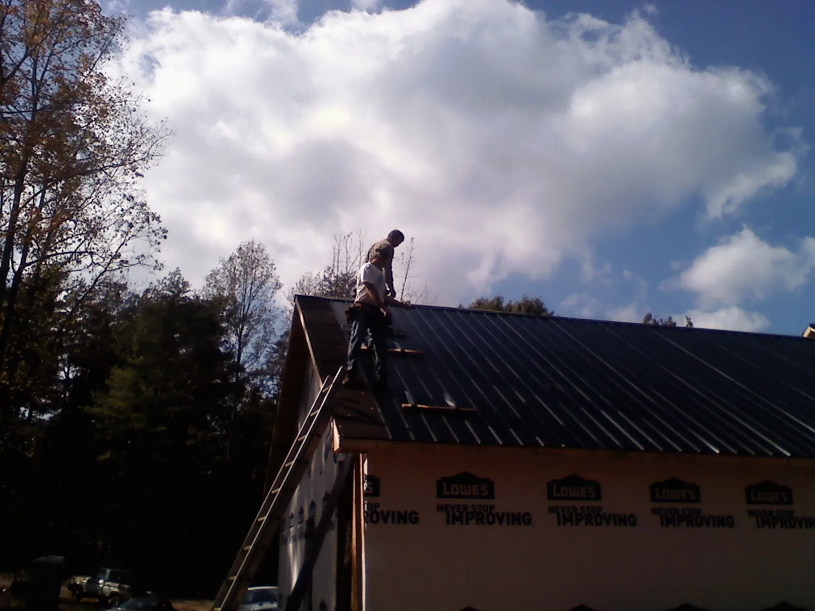 Roofer fastening dark metal panels high against a cloudy sky, from a Roof Inspection job in Clute