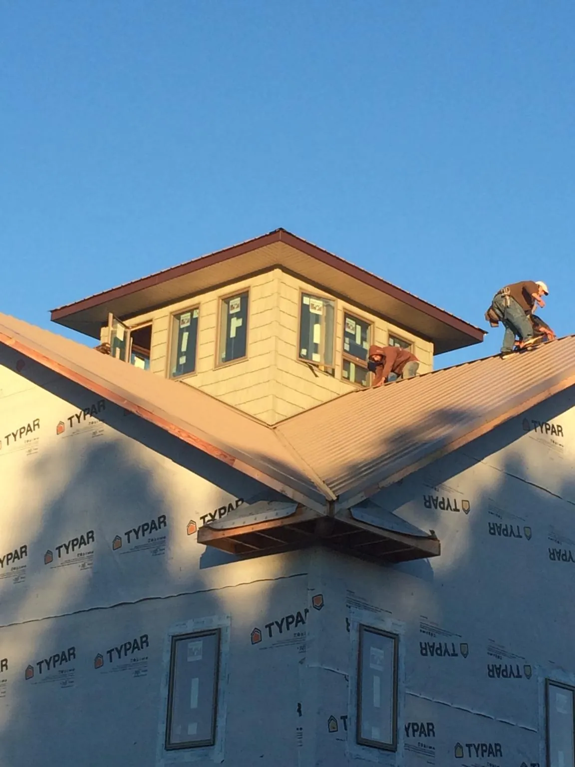 Roofers working around a rooftop cupola on a new metal roof at sunset — Roof Waterproofing in Clute by Roofing Brothers